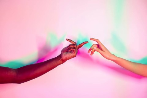 Two multiethnic hands extend toward each other against a vibrant, colorful background. The image