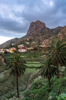 View of Roque El Cano and some houses, palm trees and landscape. Evening, cloudy sky. Vallehermoso,