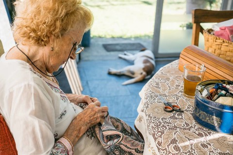 Elderly woman enjoys a peaceful afternoon sewing outdoors, her dog resting peacefully nearby,