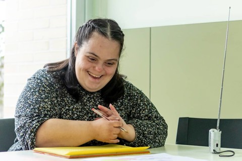 A woman enjoys a creative activity at a mental health residence, holding a pen and smiling warmly