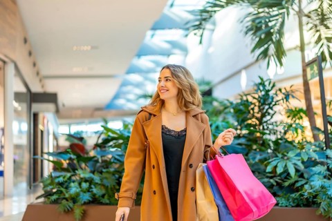 Young woman smiling while carrying colorful shopping bags. Walking through a bright. Contemporary
