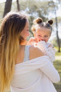 A pregnant woman shares a joyful moment with her daughter outdoors. Embracing nature, they enjoy a