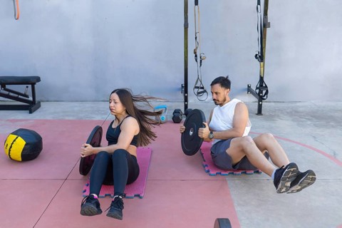 Two athletes are performing russian twists with weight plates, strengthening their core muscles in