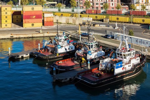 High angle view of docked red, white, blue tugboats, stacked yellow, reddish brown metal box