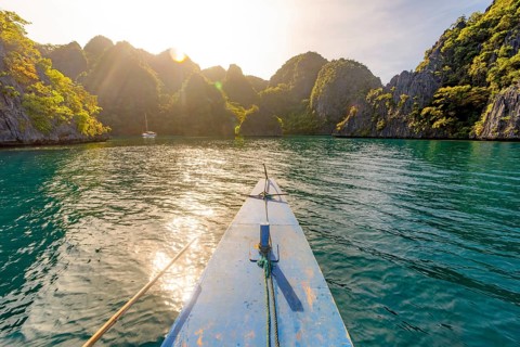 A view from a boat gliding over calm waters surrounded by lush, rocky mountains in the Philippines,