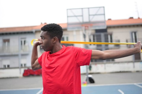 Concentrated african man warming up using elastic band in an outdoor urban basketball court
