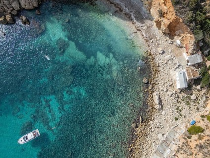 Aerial view of Costa Blanca's rocky coastline with a boat in the clear turquoise Mediterranean Sea.