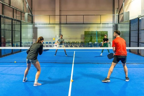 Four diverse players enjoying a competitive pickleball doubles match on a blue indoor court,