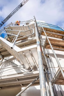 Close-up of a construction site with stairs and workers in front of a blue sky, extension of the