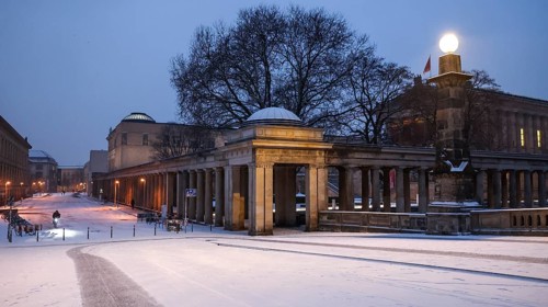 A cyclist rides over snow-covered streets at the old National Gallery in the early morning, Berlin,