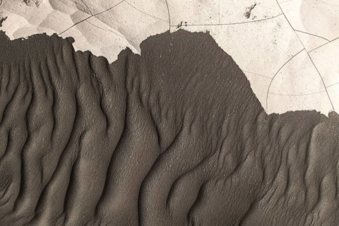 From above intricate textures of black sand shaped by natural forces on a beach. The ripples and
