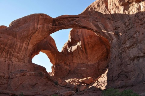 Massive double arch, called Double Arch, made of rocks under clear blue skies in a desert-like