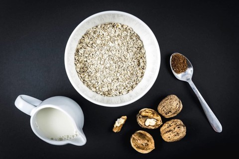 Oatmeal in a cup and winged walnuts, milk and sugar. Oatmeal recipe with walnuts, prunes, cinnamon