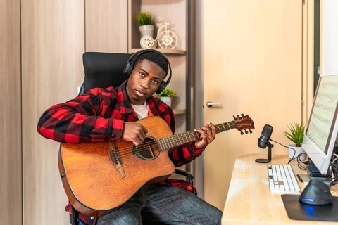 Young man playing guitar and recording music at home studio using professional microphone and