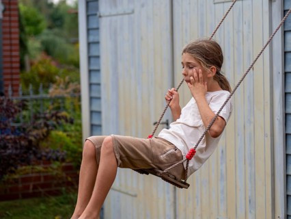 Boy swinging while sitting on children's swing at shed and garden gate, Germany