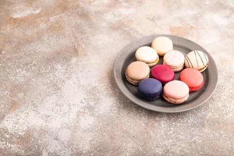 Macarons colourful cookies dessert, on brown concrete background, copy space, side view