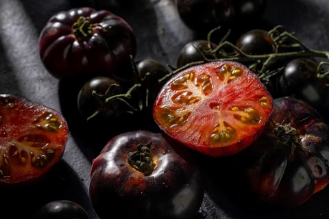 Black tomatoes, whole and sliced, display vibrant red interiors on a dark surface, illuminated by