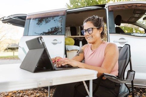 A woman works on her laptop at a portable table near her van, surrounded by the vibrant colors of