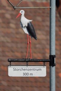 Street lamp with stork figure and sign to the stork centre 300m away, symbol for stork village,