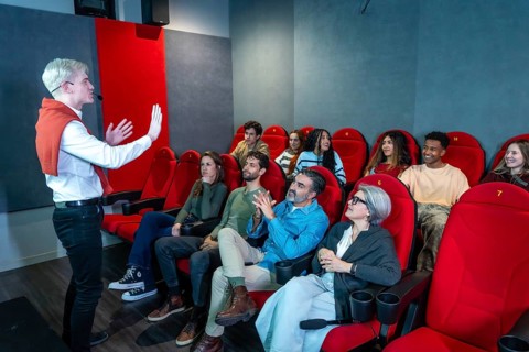 Enthusiastic speaker with microphone presenting a movie to a diverse audience in a modern cinema,