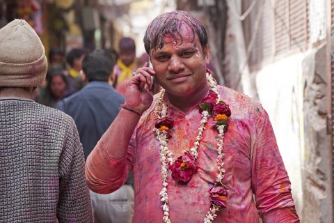 Man dyed in red with cellphone celebrating the Holi festival in Vrindavan, Uttar Pradesh, India