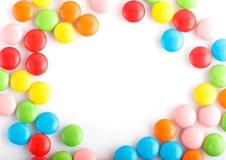 Colorful frame of multicolored chocolate candy dragees isolated on white background. Copy space.
