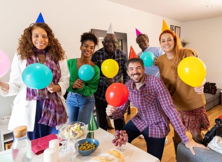 A joyful group of friends celebrating a birthday with colorful balloons and party hats indoors.