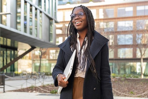 An African American businesswoman with braided hair smiling and holding a laptop while taking a
