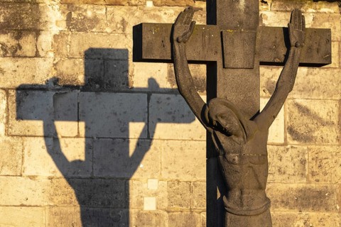 Stone cross with shadow cast at sunrise, cathedral cemetery near Cologne Cathedral, Cologne, North