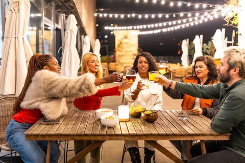 A cheerful multi-ethnic group of friends toast drinks at a night-time outdoor dining event