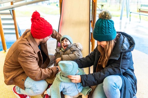 Parents and children having fun on playground slide during winter, enjoying quality family time