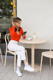 Young woman in bright orange top, sitting at an outdoor cafe in Warsaw She is engaged with her