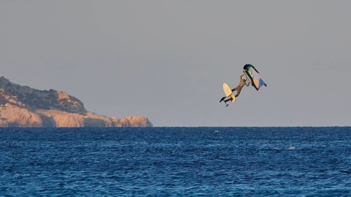 Wingfoiller, surfer jumping high over the sea with cliffs in the background in the evening light,