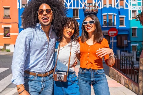 Three cheerful young tourists walking together and smiling in a vibrant, colorful street during a