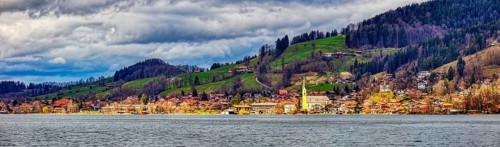 Picturesque village on the lakeshore with church, surrounded by green meadows and hills under a