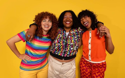 Three friends smile brightly in a colorful and cheerful setting. Standing against a vivid yellow