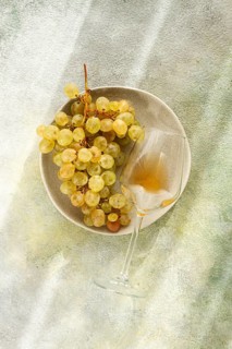 A branch of white grapes, on a gray plate, with a glass of white wine, top view, natural light,
