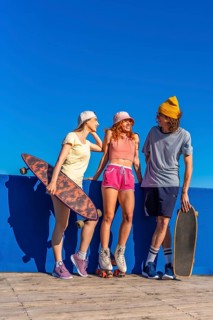 Three cheerful young friends with skateboards and roller skates are enjoying a sunny day, chatting