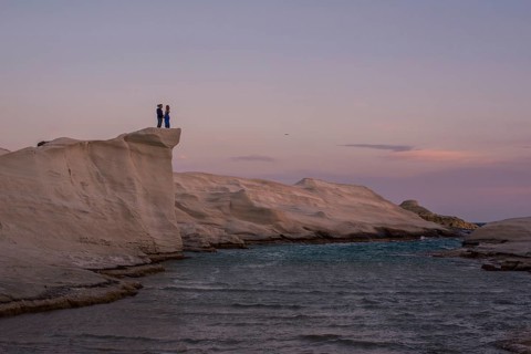 Unrecognizable couple standing on the unique white rock formations of Sarakiniko beach at sunset,