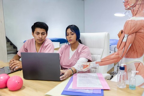 Physiotherapy clinic in Ecuador. Professionals in scrubs focus on a laptop surrounded by anatomical