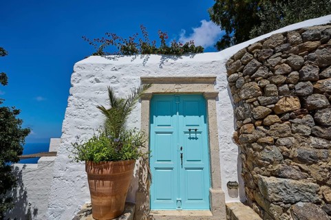Turquoise-coloured door in a white building with a plant in a clay pot and a stone wall, Chora,