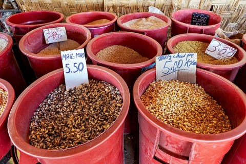 Red colored containers full of grains and legumes with price tags at a market stall, market and