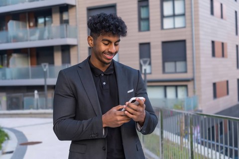 Happy and young arab businessman using phone outside a building