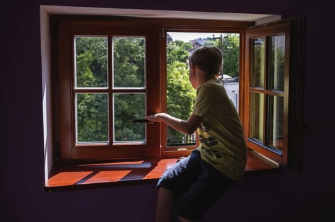 A boy sitting on a wooden sill of an open window