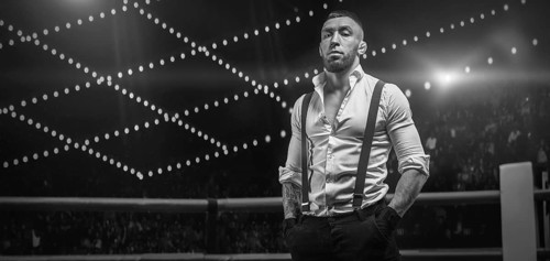 Black and white image of a bearded man in a white shirt and suspenders in the ring. The concept of