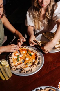 Two people share a Margherita pizza topped with mozzarella, basil, and tomato sauce. A refreshing