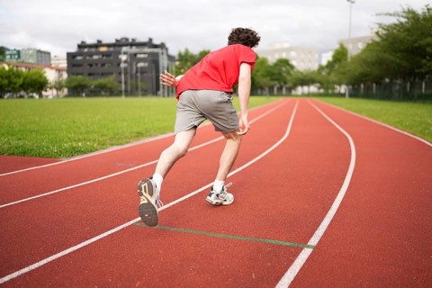 Full length rear view of a male caucasian young athlete leaving starting line in running track