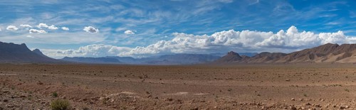 A vast desert landscape stretches out under a vibrant blue sky, with towering mountains on the