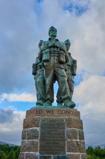 Three soldiers in a bronze statue with inscription 'United We Conquer', dramatic sky, Commando