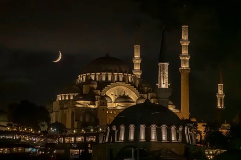 Istanbul's Suleymaniye Mosque, aglow with warm lights under a crescent moon, exemplifies majestic